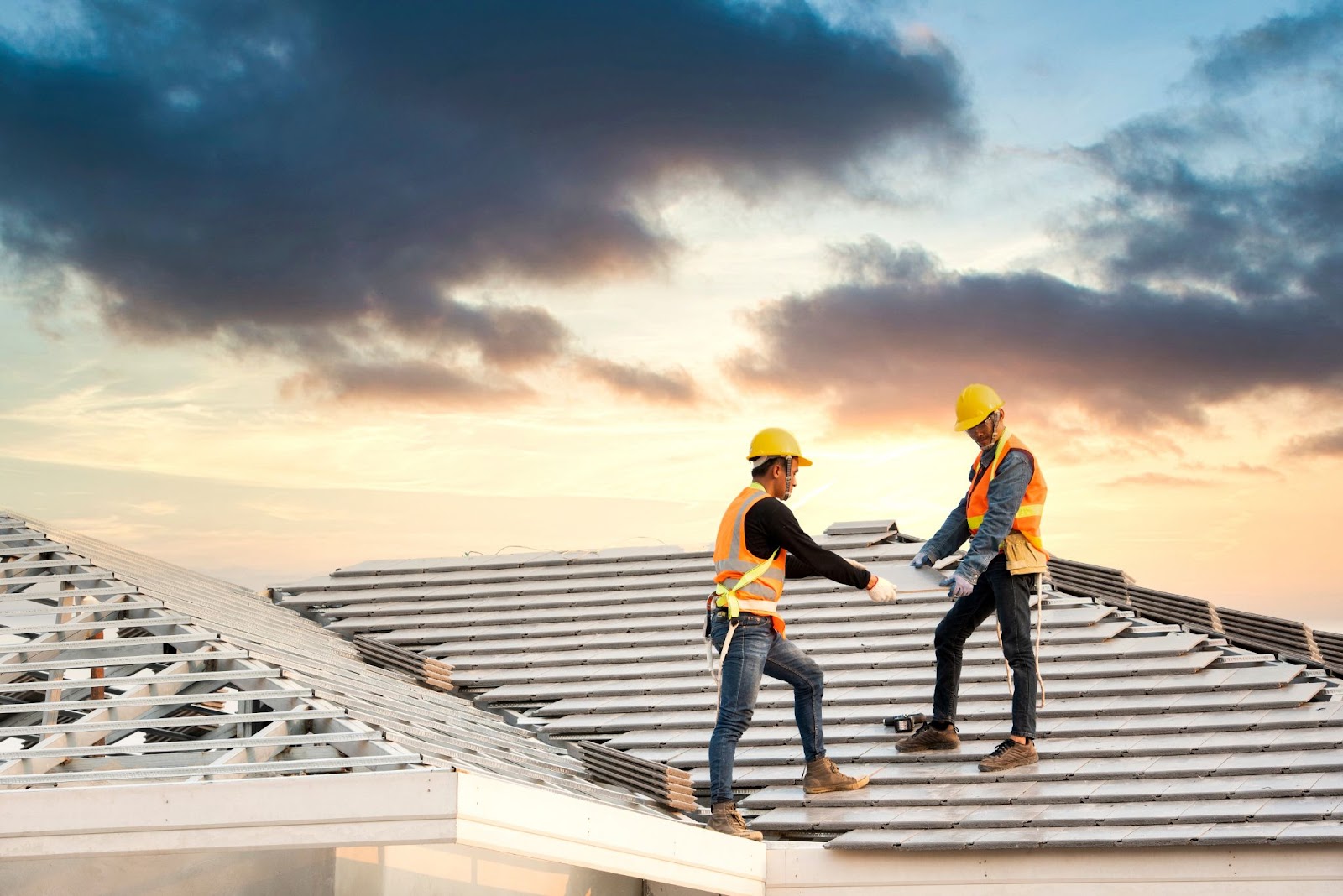 Two men in hard hats working on a new roof, preparing the house for roofing installation and maintenance.