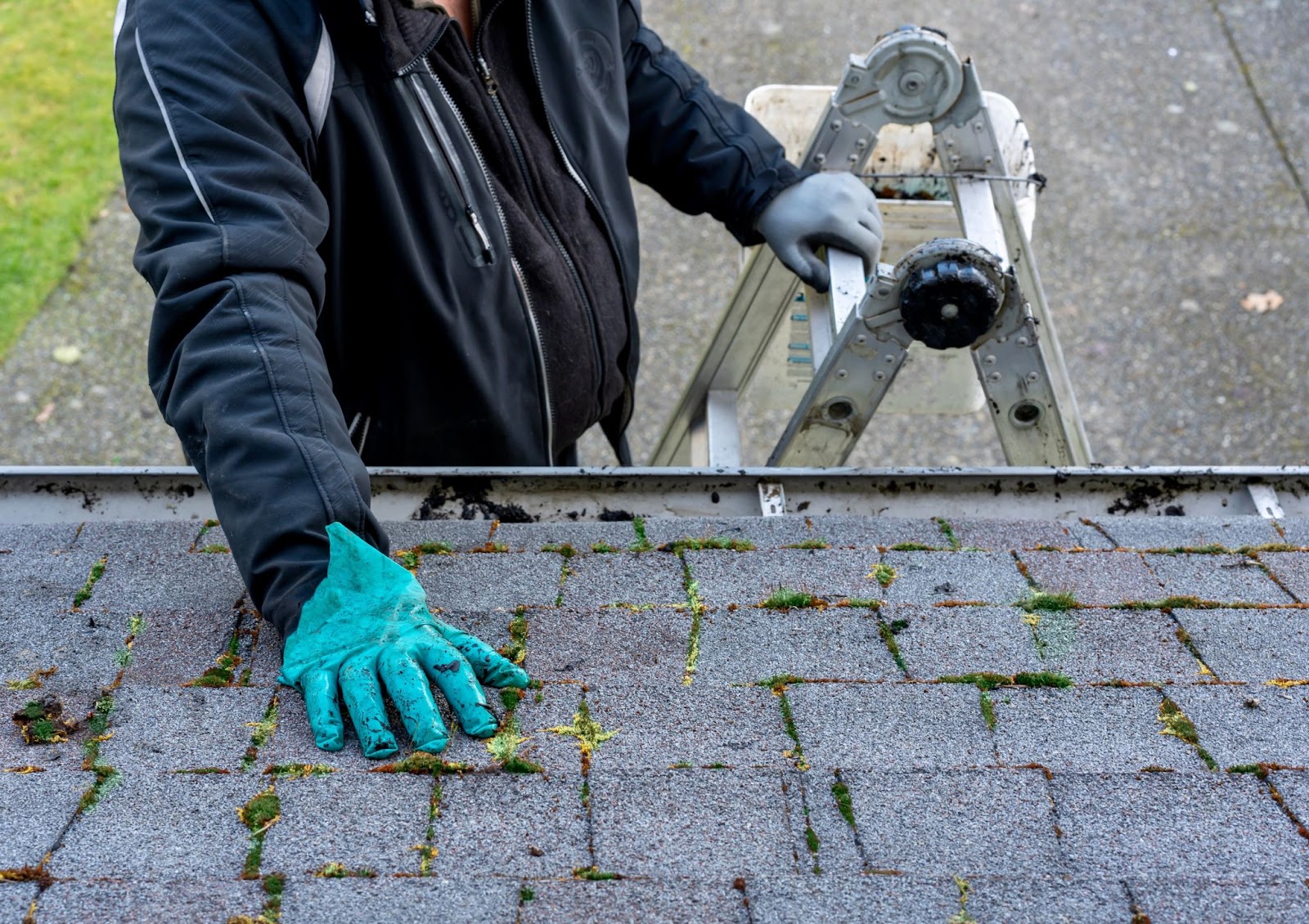 A man in gloves uses a ladder to clean a residential roof, ensuring proper maintenance and gutter cleaning in Salt Lake City.